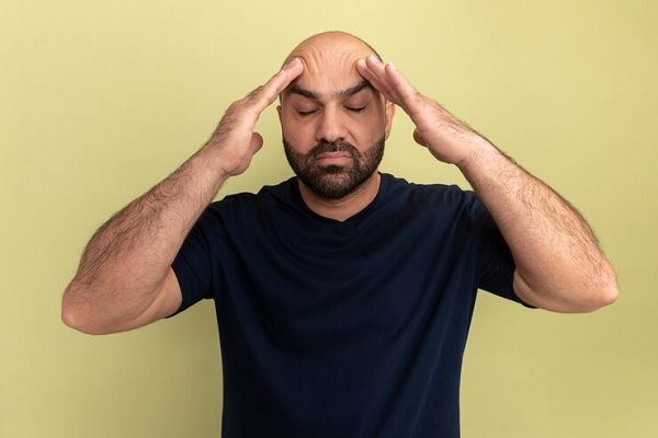 Inquiet regardant à côté d'un homme chauve d'âge moyen portant un t-shirt rose tenant les mains derrière la tête. Problèmes de santé mentale quotidiens chez les hommes et comment ils affectent les cheveux 