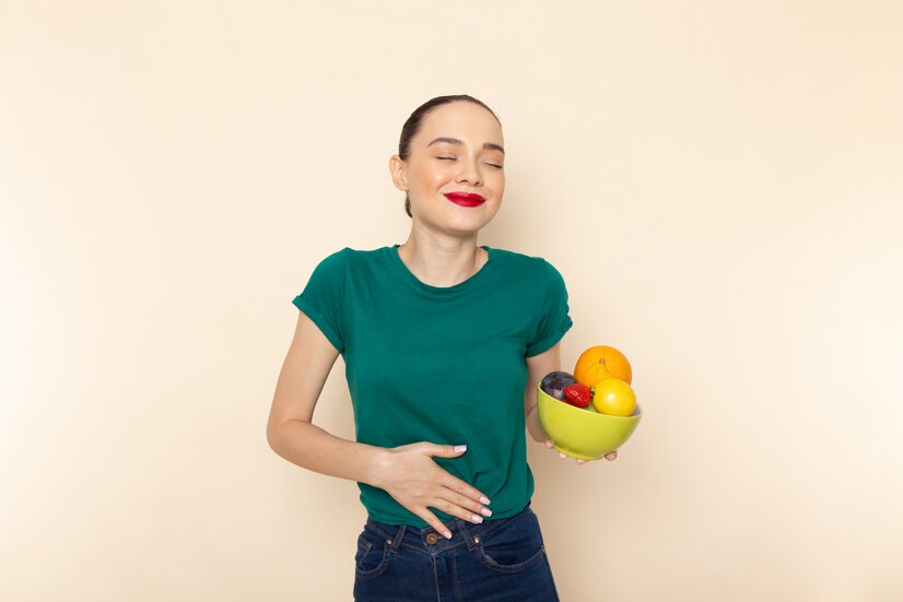 Vue de face d'une jeune femme séduisante en chemise vert foncé tenant une assiette de fruits avec un sourire. comment améliorer votre santé digestive