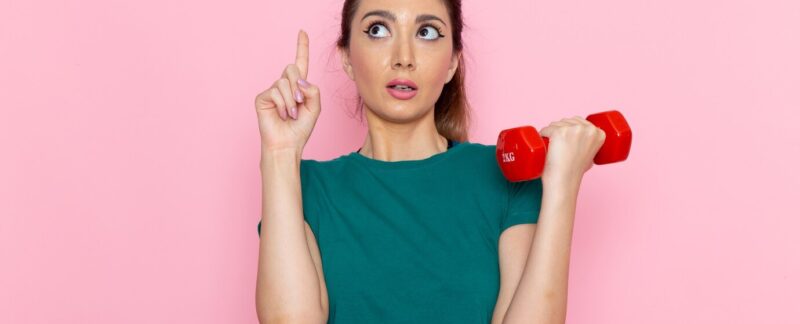 Vue de face d'une jeune femme tenant des haltères sur un mur rose, athlète, sport, exercice, santé. La créatine, qu'est-ce que c'est et à quoi ça sert