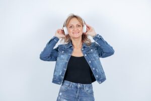 Une jeune fille souriante avec des écouteurs regarde vers le haut sur un fond blanc. 