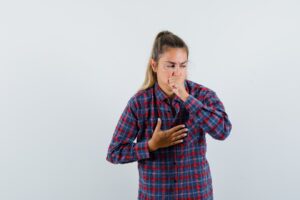 Jeune femme en chemise à carreaux souffrant de toux et ayant l'air malade, vue de face.