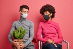 Un jeune couple se regarde tristement porter des masques pendant la quarantaine à la maison poser sur des chaises éviter la contagion et rester en sécurité porter un cactus en pot. 
