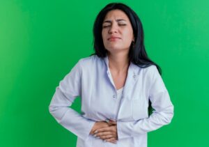 Jeune femme médecin en robe de chambre se tenant le ventre les yeux fermés. 