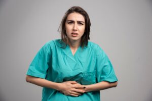 Femme médecin souffrant de maux d'estomac sur fond gris. Photo de haute qualité.