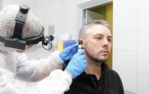 Photo de profil d'un oto-rhino-laryngologiste tenant un otoscope sur l'oreille d'un patient, lors d'un examen. otite