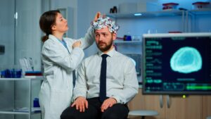 Patient ayant passé un scanner cérébral et discutant avec un chercheur en neurologie tout en ajustant un casque de balayage des ondes cérébrales, examinant le diagnostic de la maladie, expliquant les résultats de l'EEG, l'état de santé et les fonctions cérébrales.