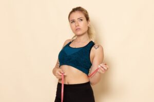 Vue de face d'une jeune femme en tenue de sport mesurant sa taille et son tour de taille.