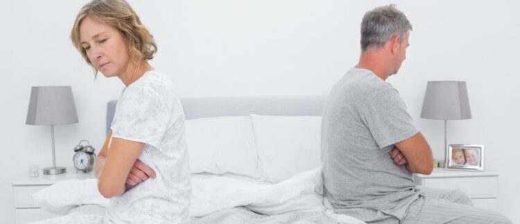 Couple assis de part et d'autre du lit et ne se parlant pas après une dispute. Incontinence urinaire chez l'homme et la femme