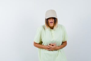 Jeune femme en T-shirt et casquette souffrant de maux d'estomac et ayant l'air malade, vue de face.
