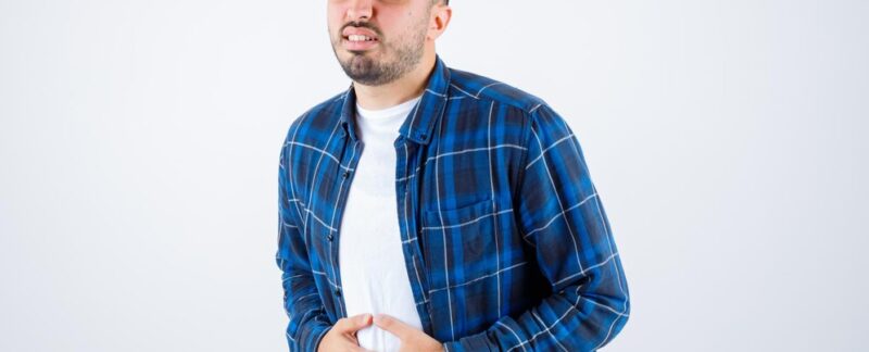 Un jeune homme souffrant de maux de ventre, vêtu d'une chemise à carreaux et d'un tee-shirt blanc, semble épuisé. Peut-on mourir d'un reflux gastrique