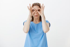 Une femme mignonne et idiote qui regarde à travers des lunettes, avec des gestes corrects.