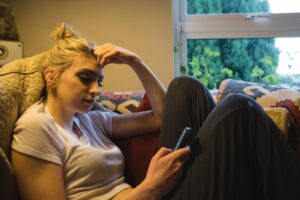 Femme assise et utilisant un téléphone portable sur le canapé du salon. Quelles sont les causes de la paralysie du sommeil