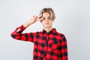 Jeune adolescent en chemise à carreaux montrant le signe V près de l'œil et ayant l'air confiant.