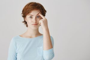 Une fille rousse surprise et émerveillée pose contre le mur blanc.