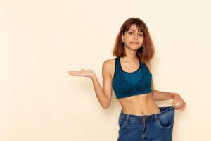Vue de face d'une jeune femme en bonne forme physique, vêtue d'une chemise bleue, souriant sur un mur blanc clair.