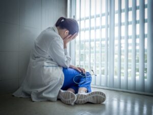 Médecin dépressif assis en désespoir de cause près d'une fenêtre d'hôpital : concept de soins médicaux et de douleur.