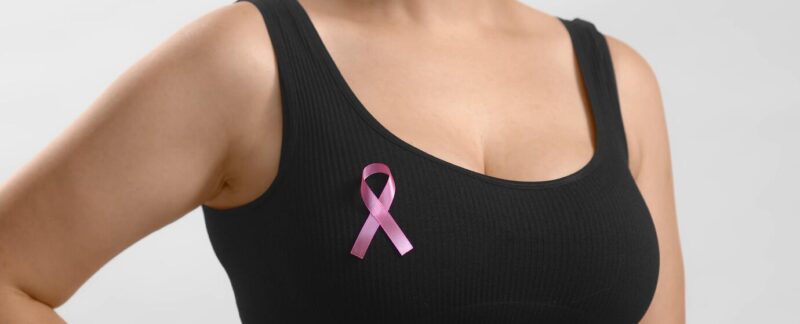 Jeune fille européenne vêtue d'un haut noir, debout, avec un ruban sur la poitrine en signe de soutien au cancer du sein.
