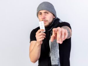 Jeune homme caucasien malade et mécontent, portant un bonnet d'hiver et une écharpe, tenant un sac à dos. la toxicomanie