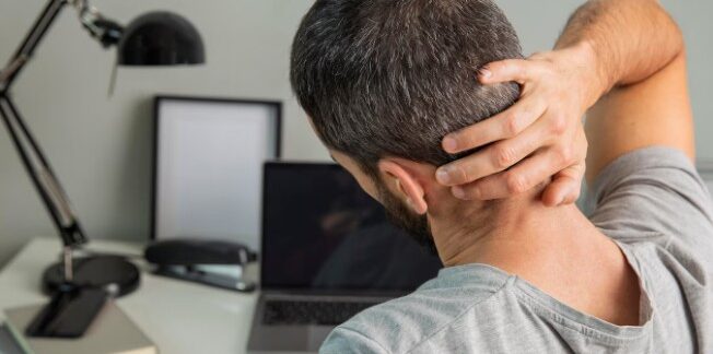 Vue de dos d'un homme s'étirant tout en travaillant à domicile. Troubles musculo-squelettiques, voici les plus courants